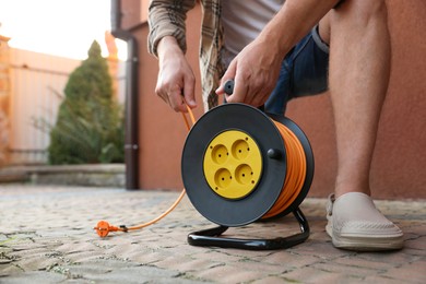 Photo of Man with extension cord reel in backyard, closeup. Space for text