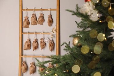 Advent calendar with gifts hanging on white wall near Christmas tree indoors