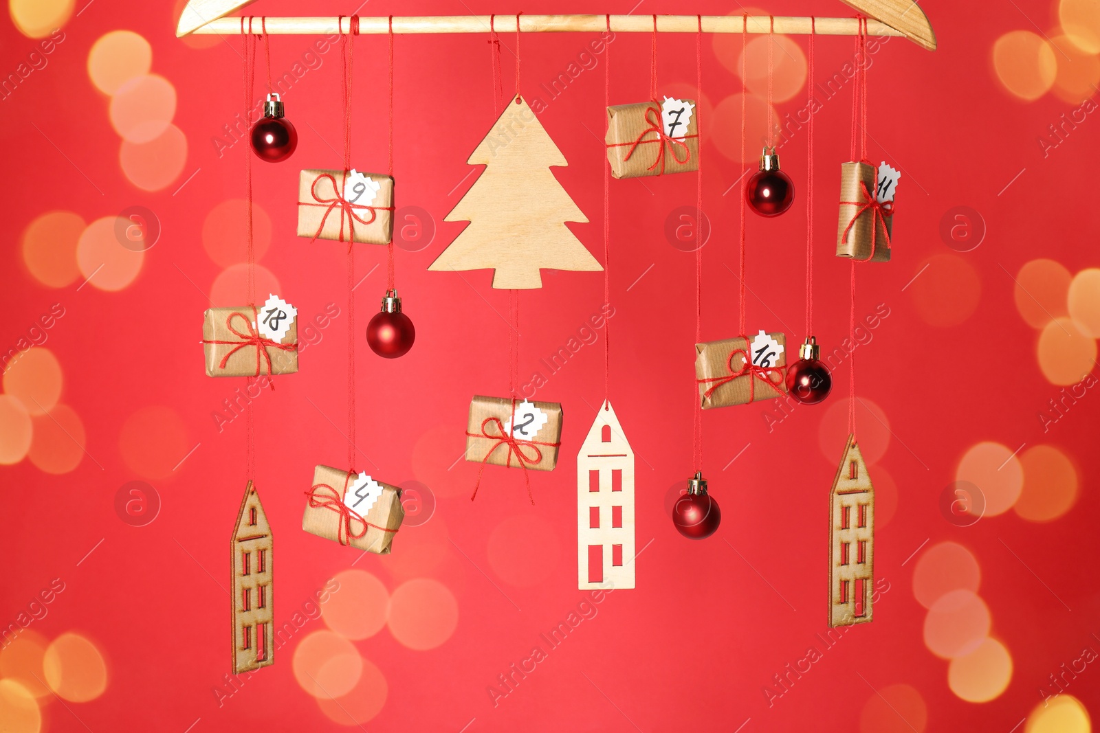 Photo of Handmade advent calendar and decor hanging on red background with blurred lights