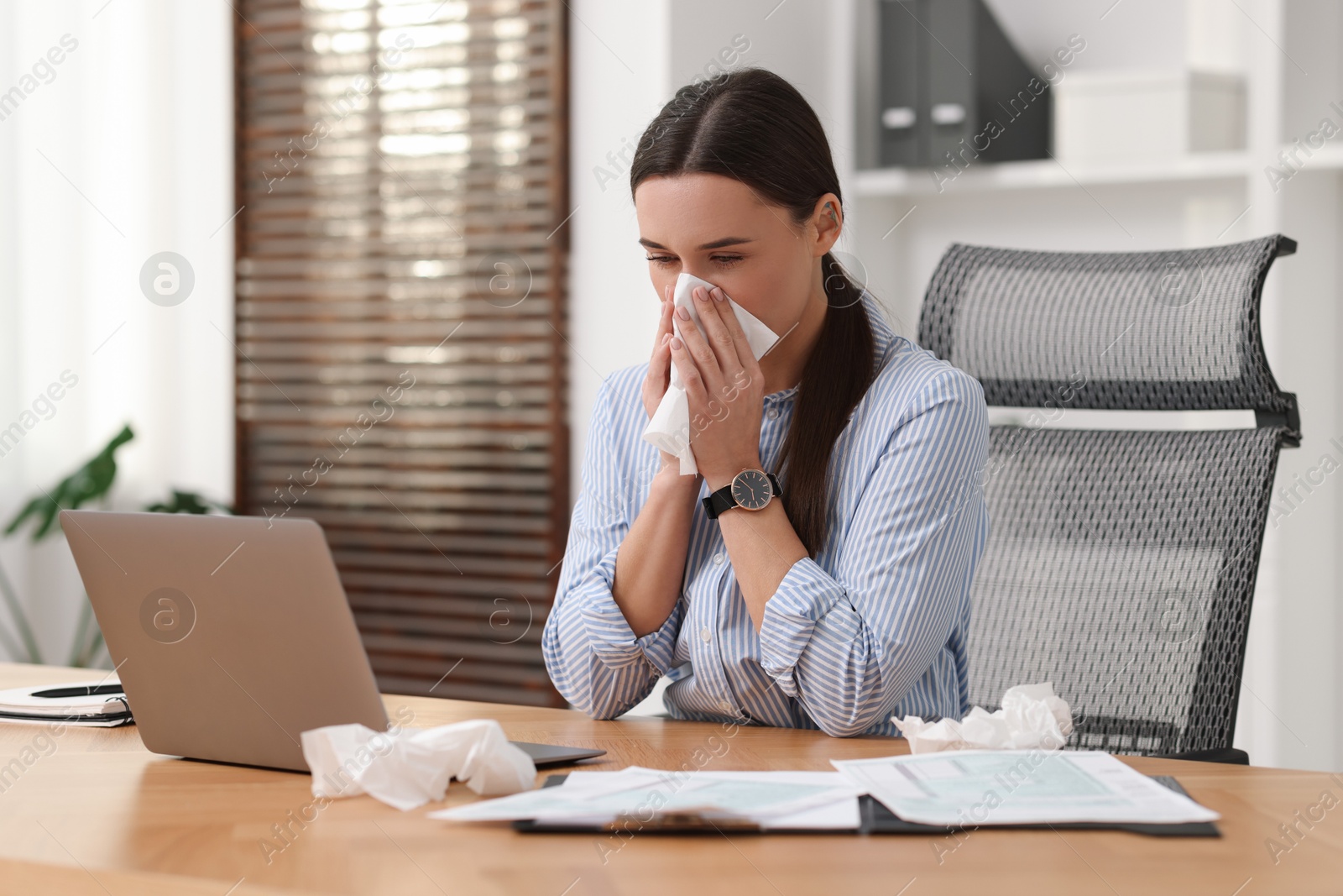 Photo of Sick woman with runny nose at table in office