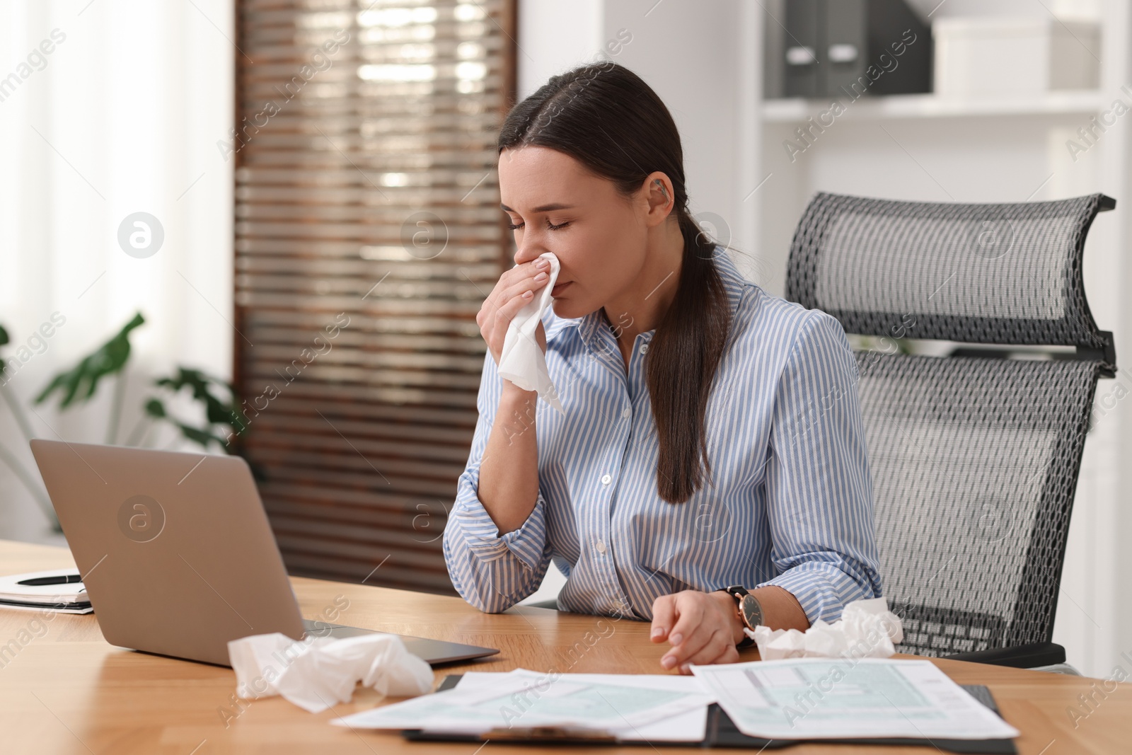 Photo of Sick woman with runny nose at table in office