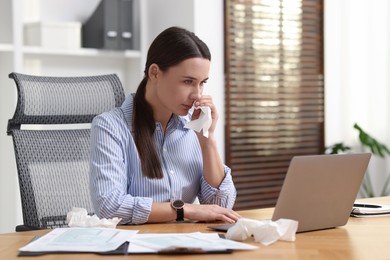 Photo of Sick woman with runny nose at table in office