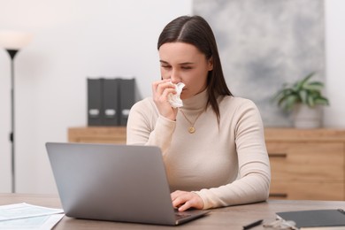 Photo of Sick woman with runny nose working at table in office