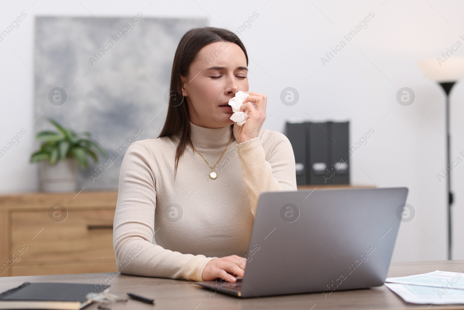 Photo of Sick woman with runny nose working at table in office