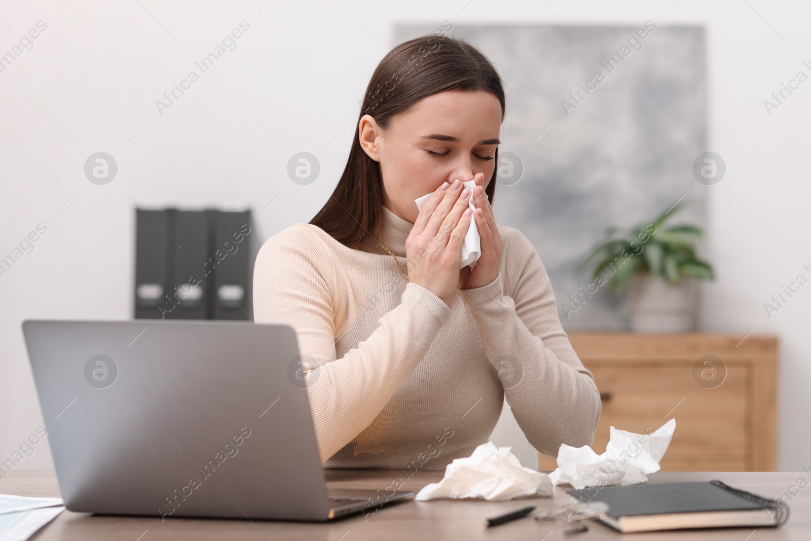 Photo of Sick woman with runny nose at table in office