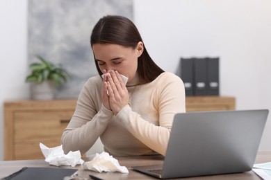 Photo of Sick woman with runny nose at table in office