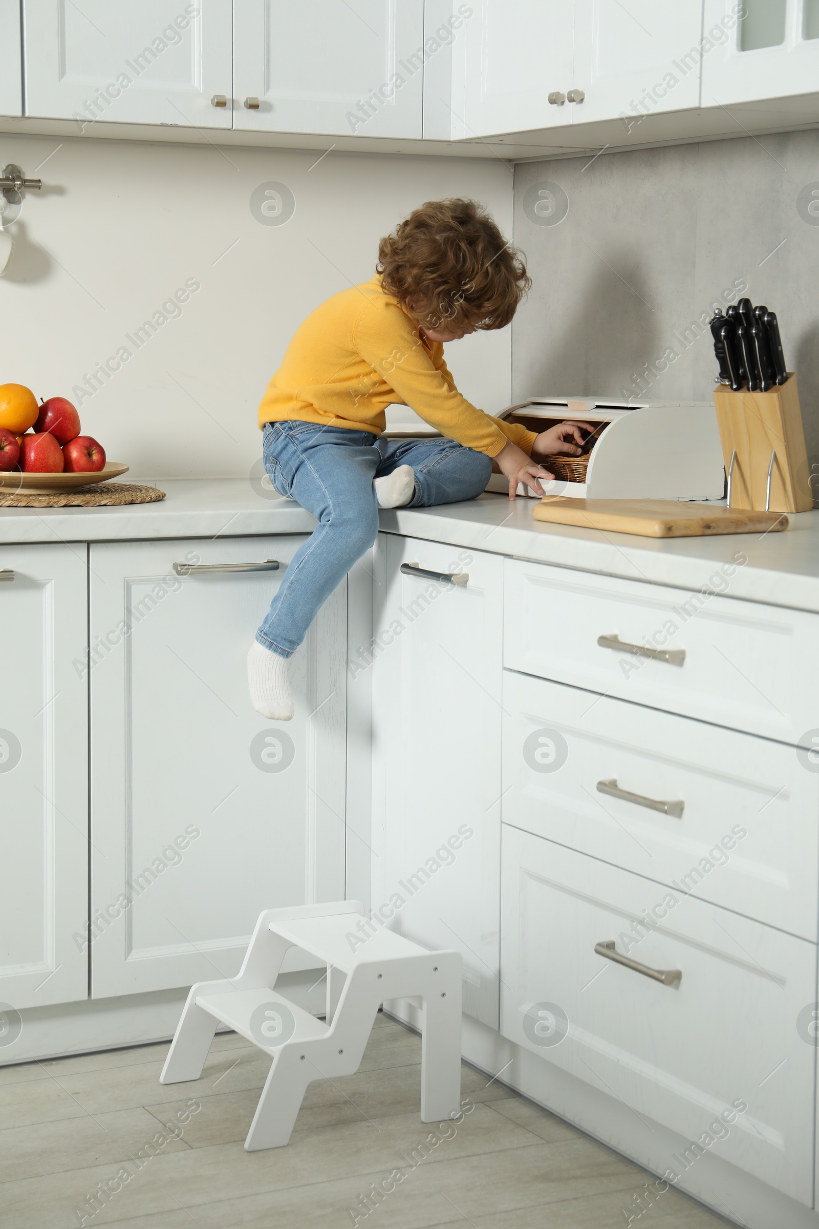 Photo of Little boy taking cookie on countertop and step stool in kitchen