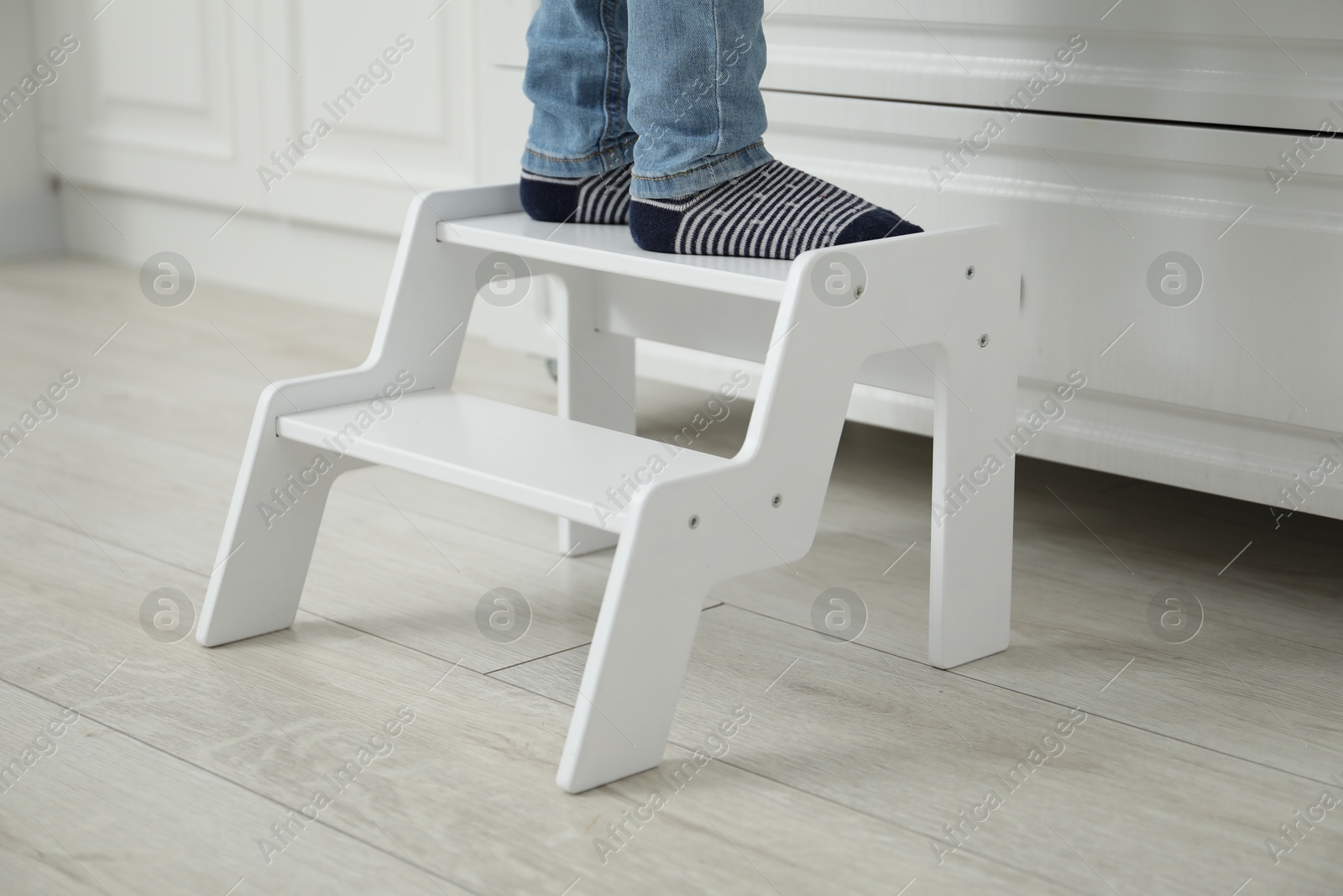 Photo of Little boy standing on step stool at home, closeup