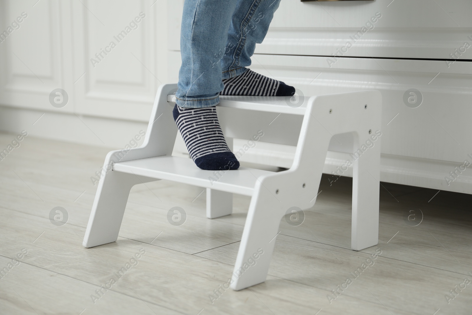 Photo of Little boy standing on step stool at home, closeup