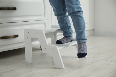 Photo of Little boy with step stool near chest of drawers at home, closeup