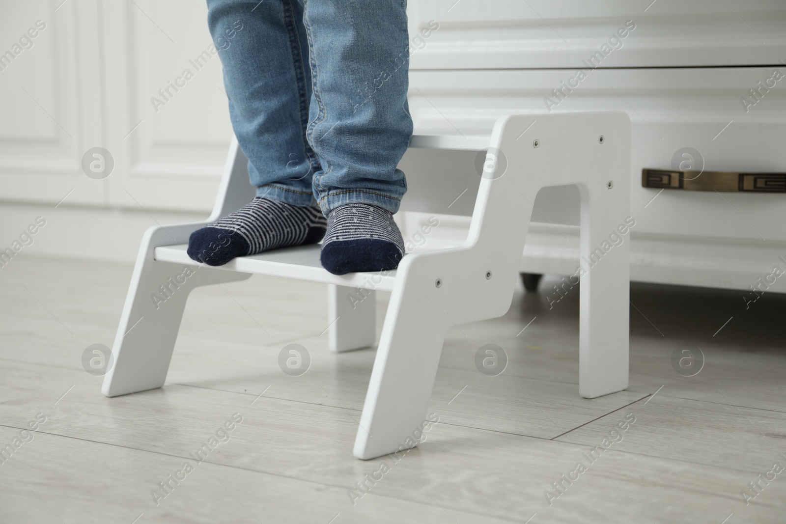 Photo of Little boy with step stool near chest of drawers at home, closeup