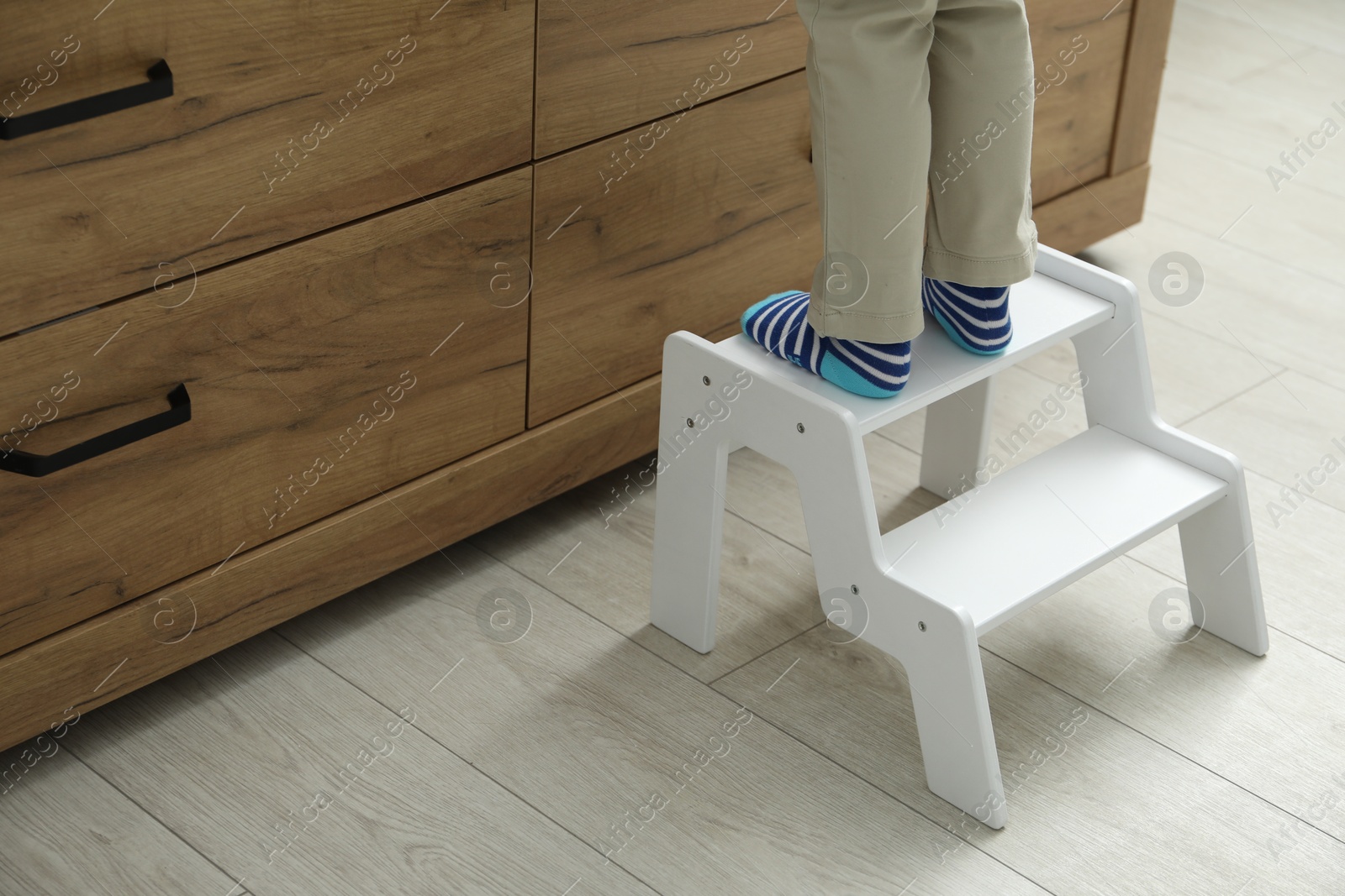 Photo of Little boy with step stool near chest of drawers at home, closeup