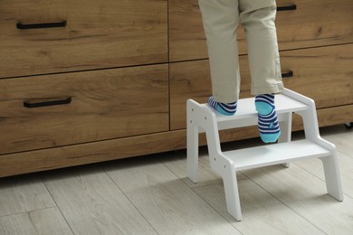 Photo of Little boy with step stool near chest of drawers at home, closeup