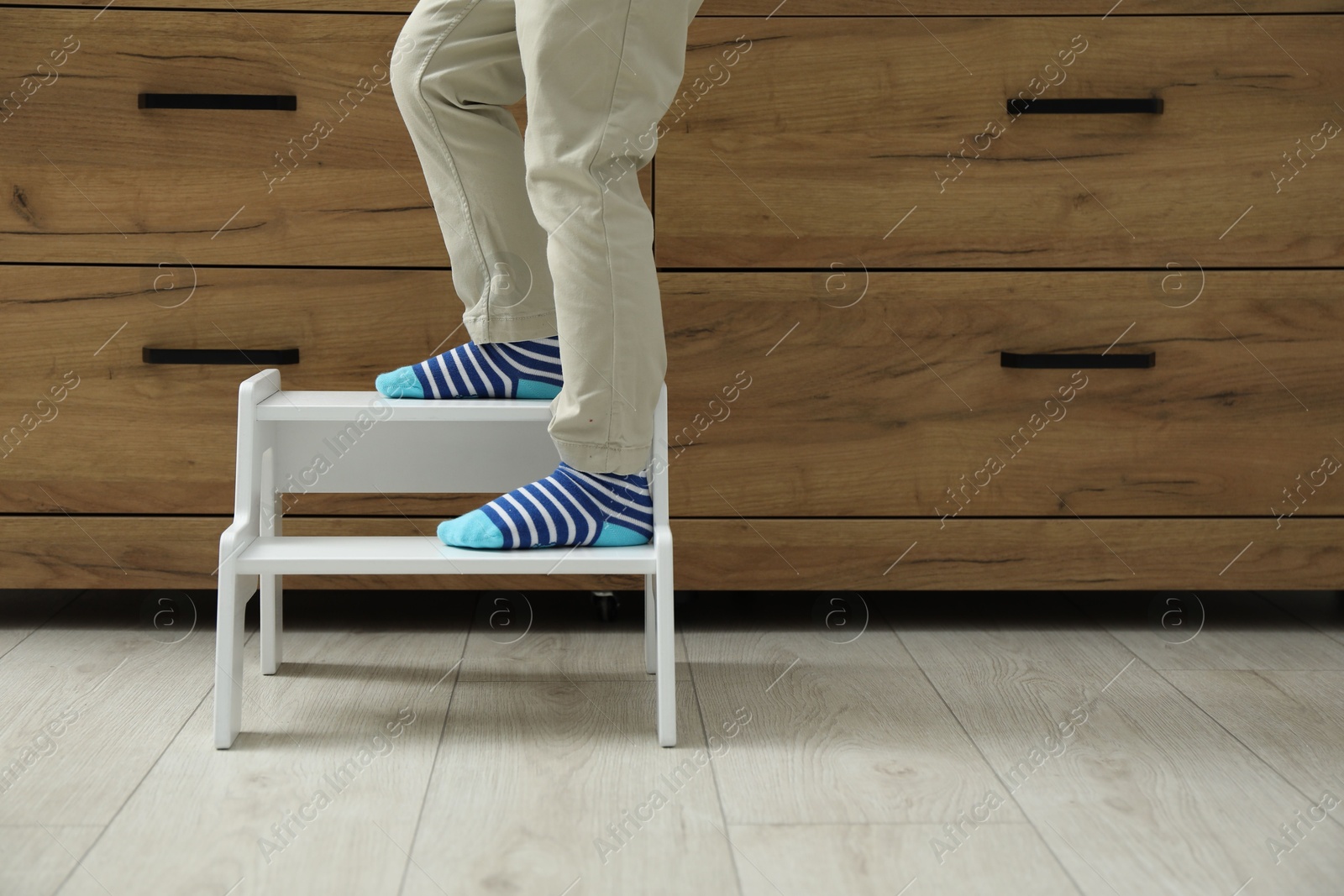 Photo of Little boy with step stool near chest of drawers at home, closeup