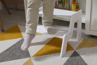 Photo of Little boy standing on step stool at home, closeup