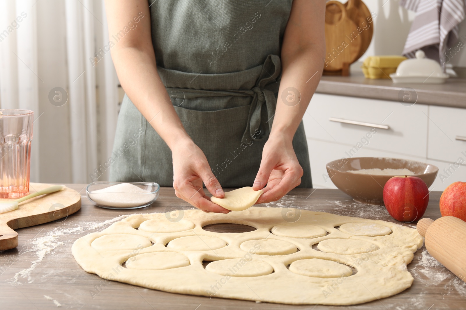 Photo of Woman making pirozhki (stuffed pastry pies) at wooden table indoors, closeup