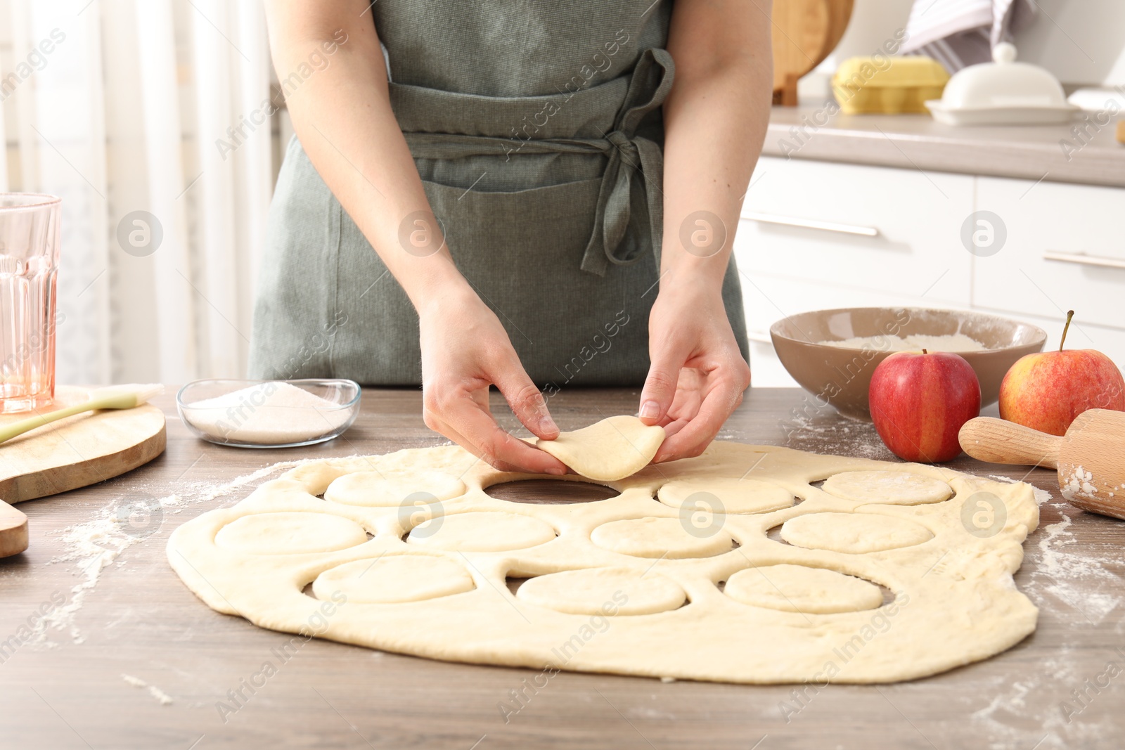 Photo of Woman making pirozhki (stuffed pastry pies) at wooden table indoors, closeup