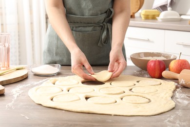 Photo of Woman making pirozhki (stuffed pastry pies) at wooden table indoors, closeup