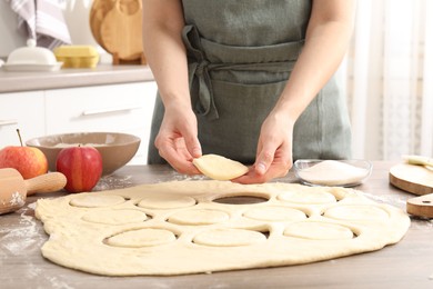 Photo of Woman making pirozhki (stuffed pastry pies) at wooden table indoors, closeup