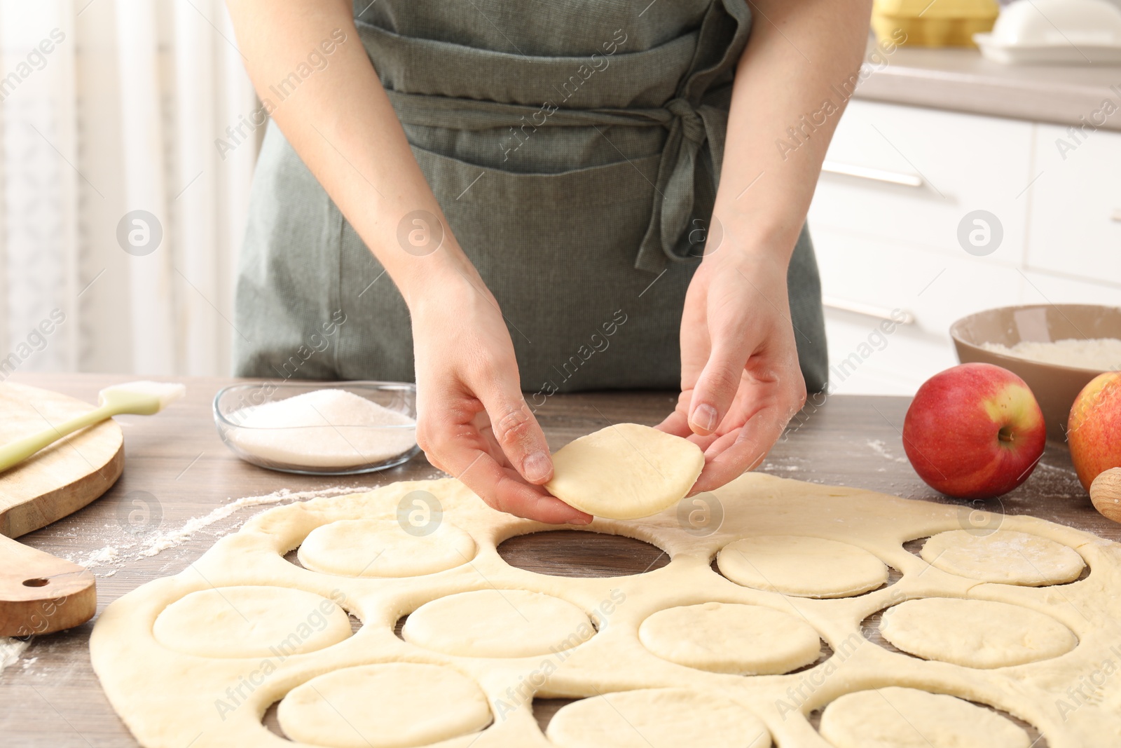 Photo of Woman making pirozhki (stuffed pastry pies) at wooden table indoors, closeup