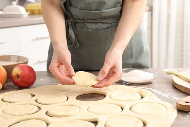 Photo of Woman making pirozhki (stuffed pastry pies) at wooden table indoors, closeup