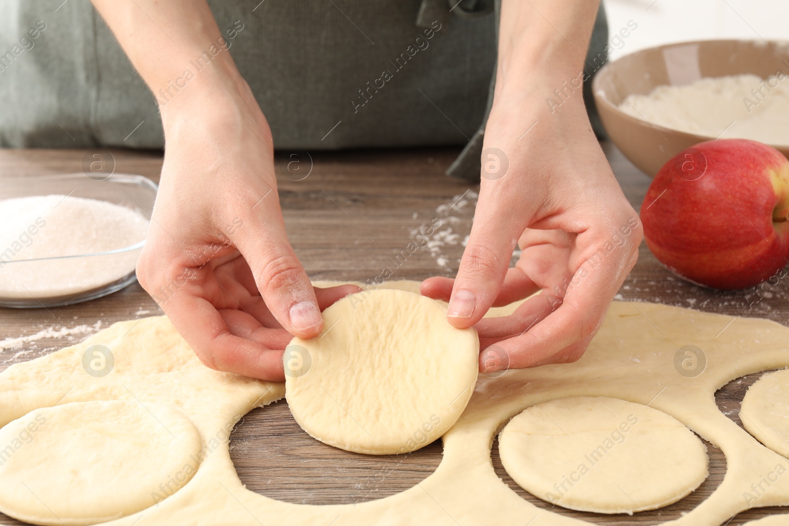 Photo of Woman making pirozhki (stuffed pastry pies) at wooden table, closeup