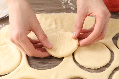 Photo of Woman making pirozhki (stuffed pastry pies) at wooden table, closeup