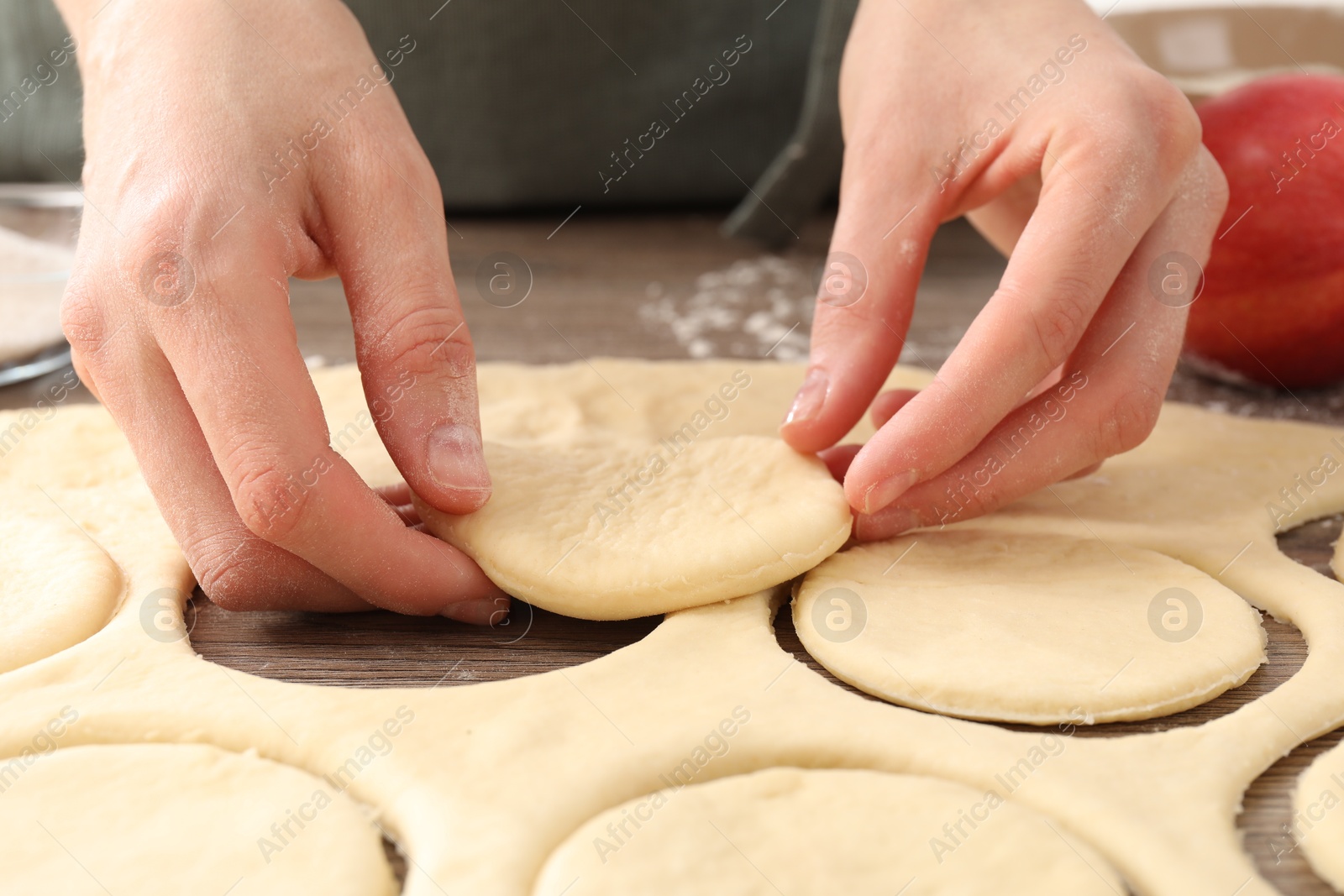 Photo of Woman making pirozhki (stuffed pastry pies) at wooden table, closeup