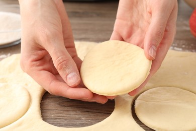 Photo of Woman making pirozhki (stuffed pastry pies) at wooden table, closeup