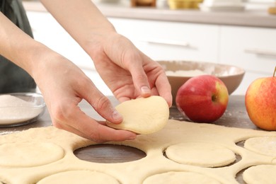 Photo of Woman making pirozhki (stuffed pastry pies) at wooden table indoors, closeup