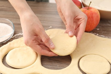 Photo of Woman making pirozhki (stuffed pastry pies) at wooden table, closeup