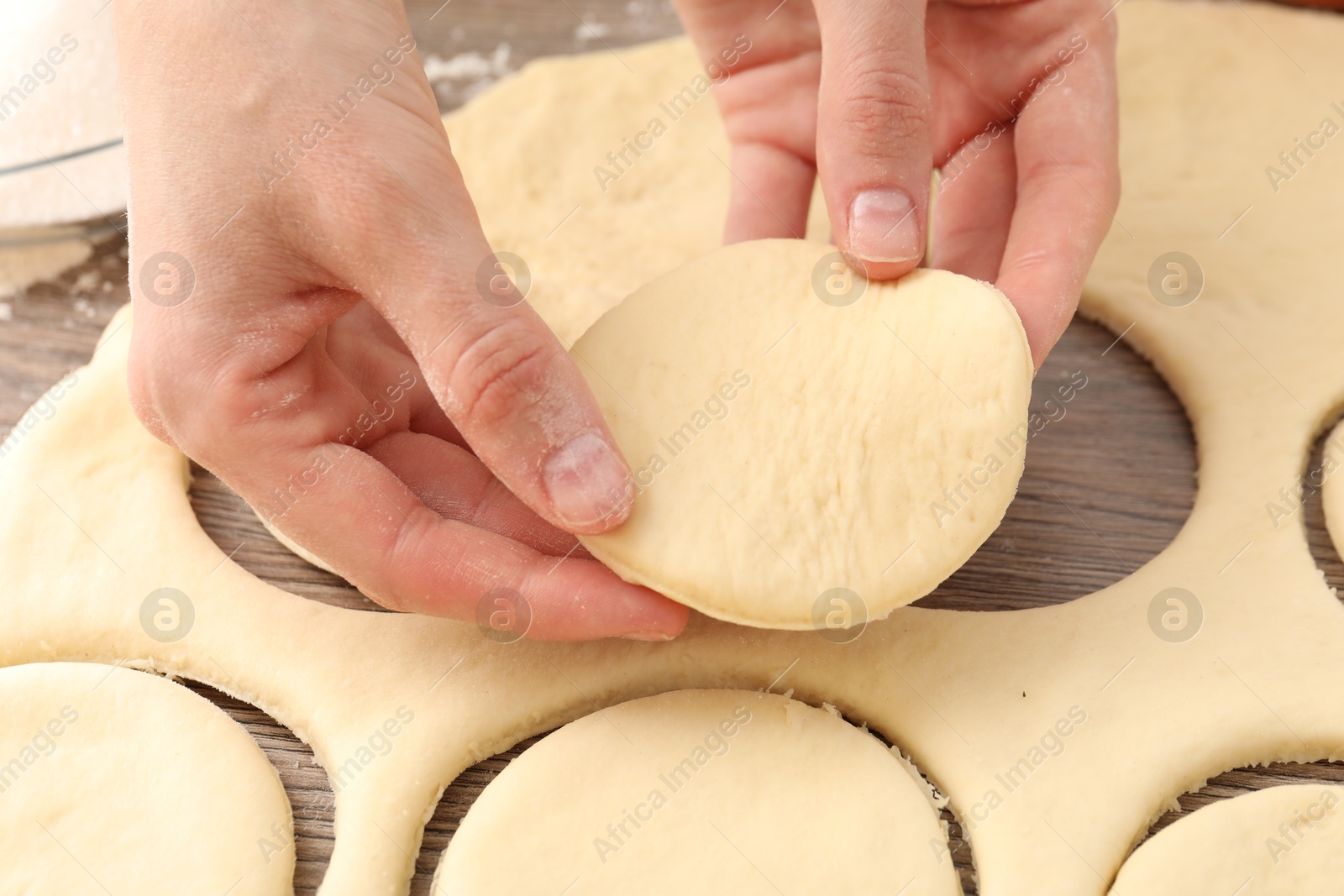 Photo of Woman making pirozhki (stuffed pastry pies) at wooden table, closeup