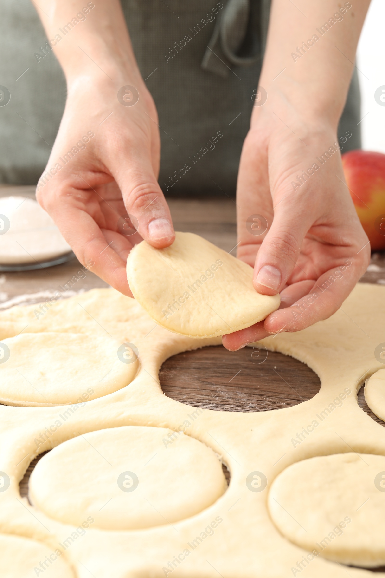 Photo of Woman making pirozhki (stuffed pastry pies) at wooden table, closeup