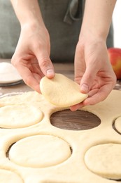 Photo of Woman making pirozhki (stuffed pastry pies) at wooden table, closeup