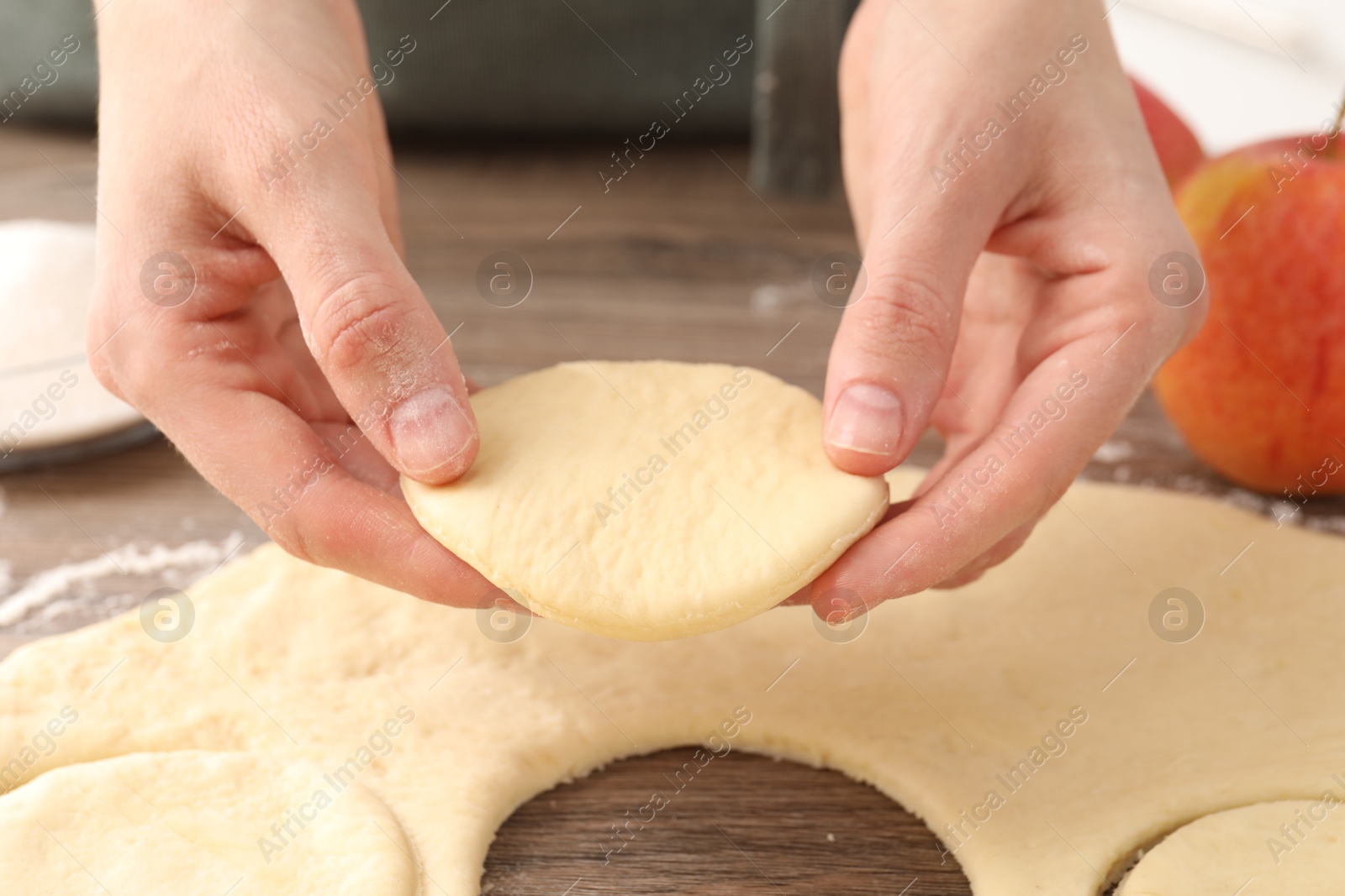 Photo of Woman making pirozhki (stuffed pastry pies) at wooden table, closeup