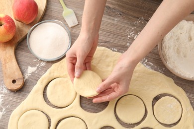 Photo of Woman making pirozhki (stuffed pastry pies) at wooden table, top view