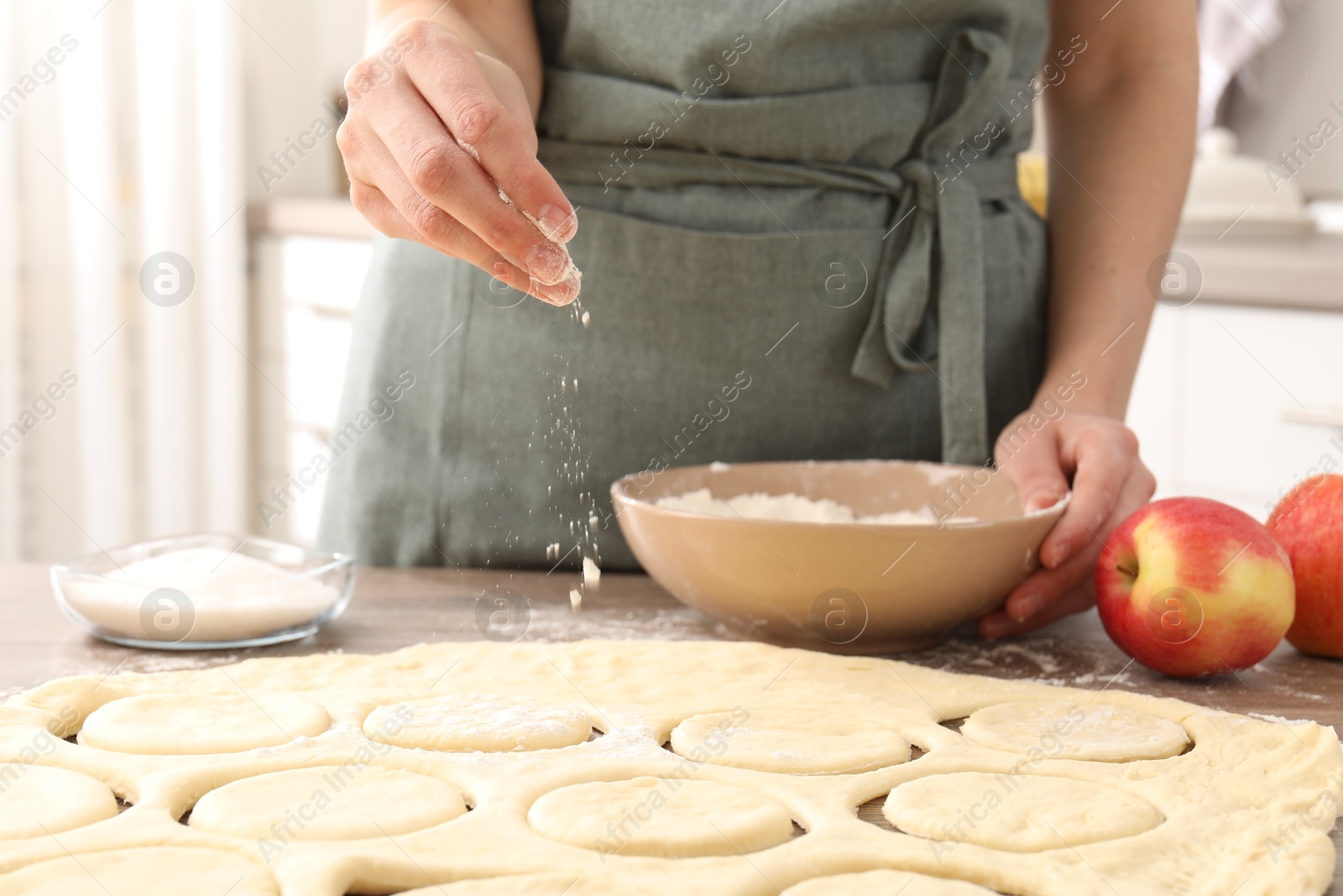 Photo of Woman making pirozhki (stuffed pastry pies) at wooden table indoors, closeup