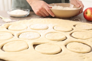 Photo of Woman making pirozhki (stuffed pastry pies) at wooden table indoors, closeup