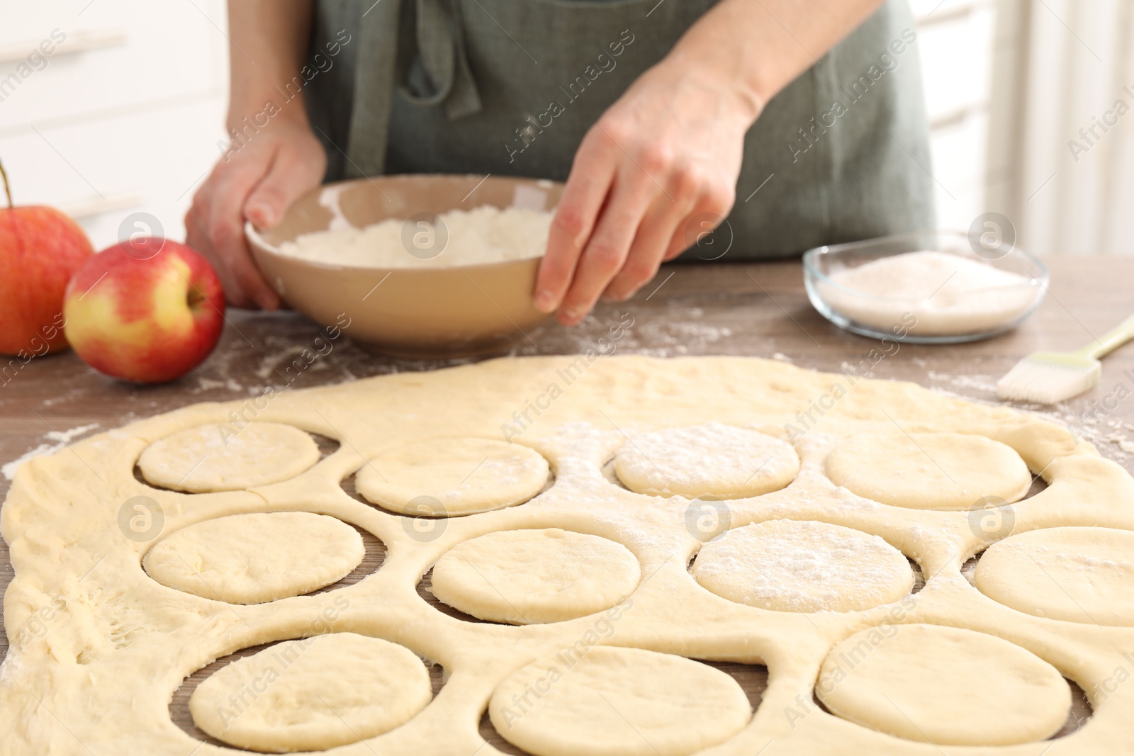 Photo of Woman making pirozhki (stuffed pastry pies) at wooden table indoors, closeup