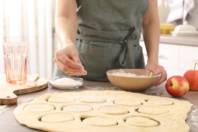 Photo of Woman making pirozhki (stuffed pastry pies) at wooden table indoors, closeup