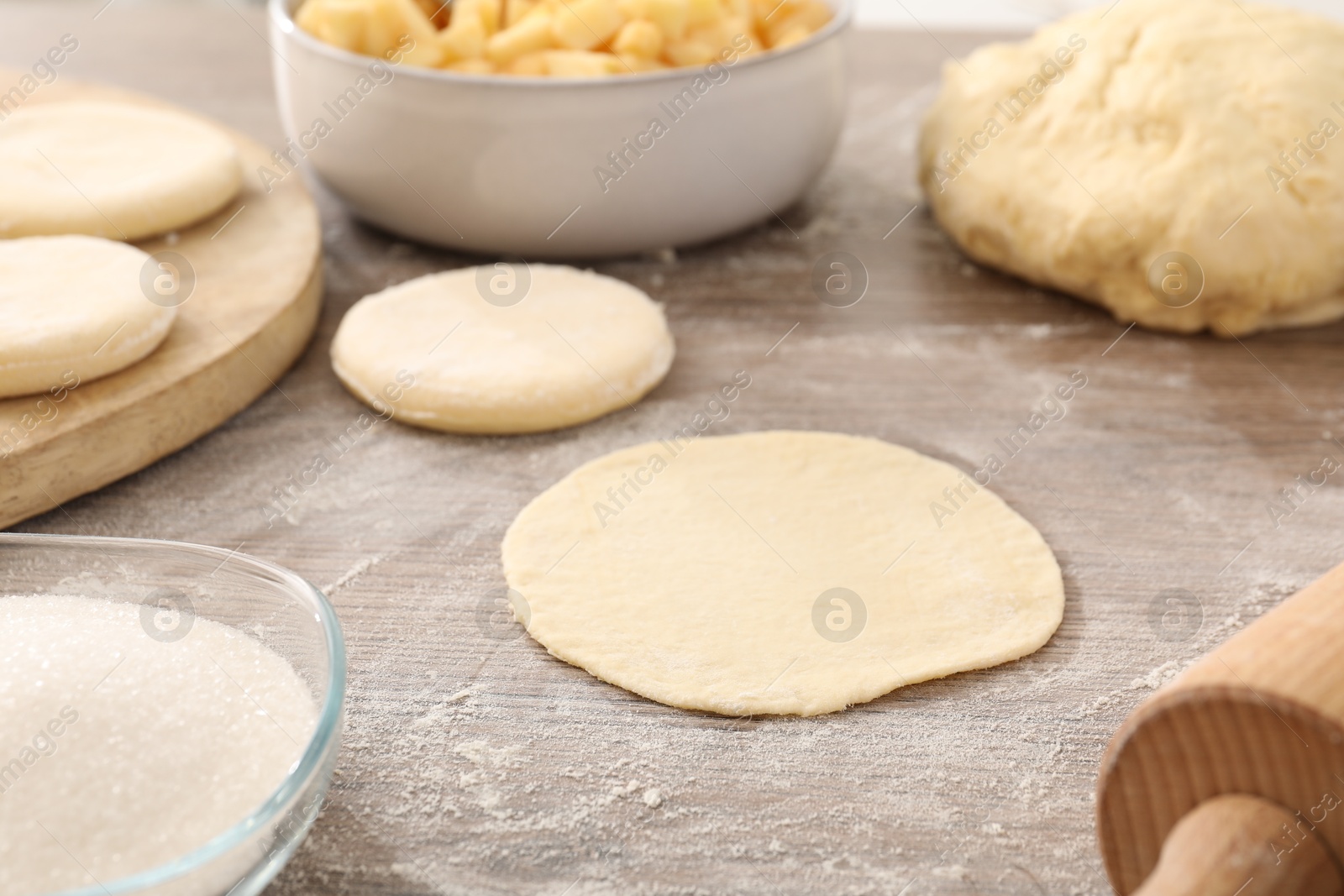 Photo of Making pirozhki (stuffed pastry pies). Pieces of dough on wooden table, closeup