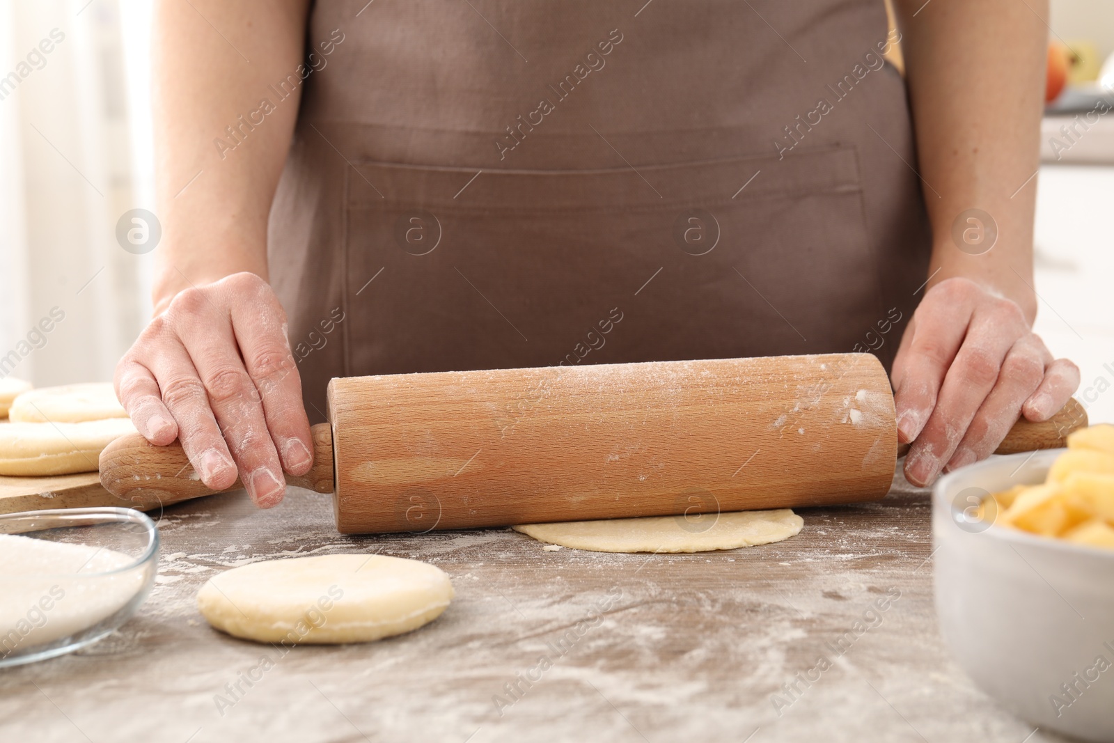 Photo of Making pirozhki (stuffed pastry pies). Woman shaping dough with rolling pin at wooden table, closeup