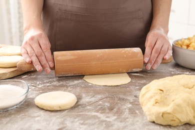 Photo of Making pirozhki (stuffed pastry pies). Woman shaping dough with rolling pin at wooden table, closeup