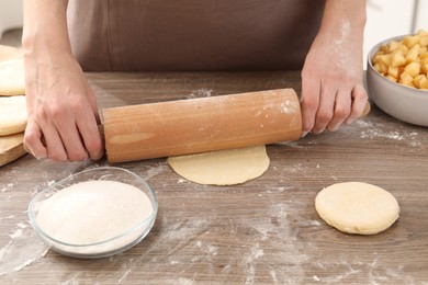 Photo of Making pirozhki (stuffed pastry pies). Woman shaping dough with rolling pin at wooden table, closeup