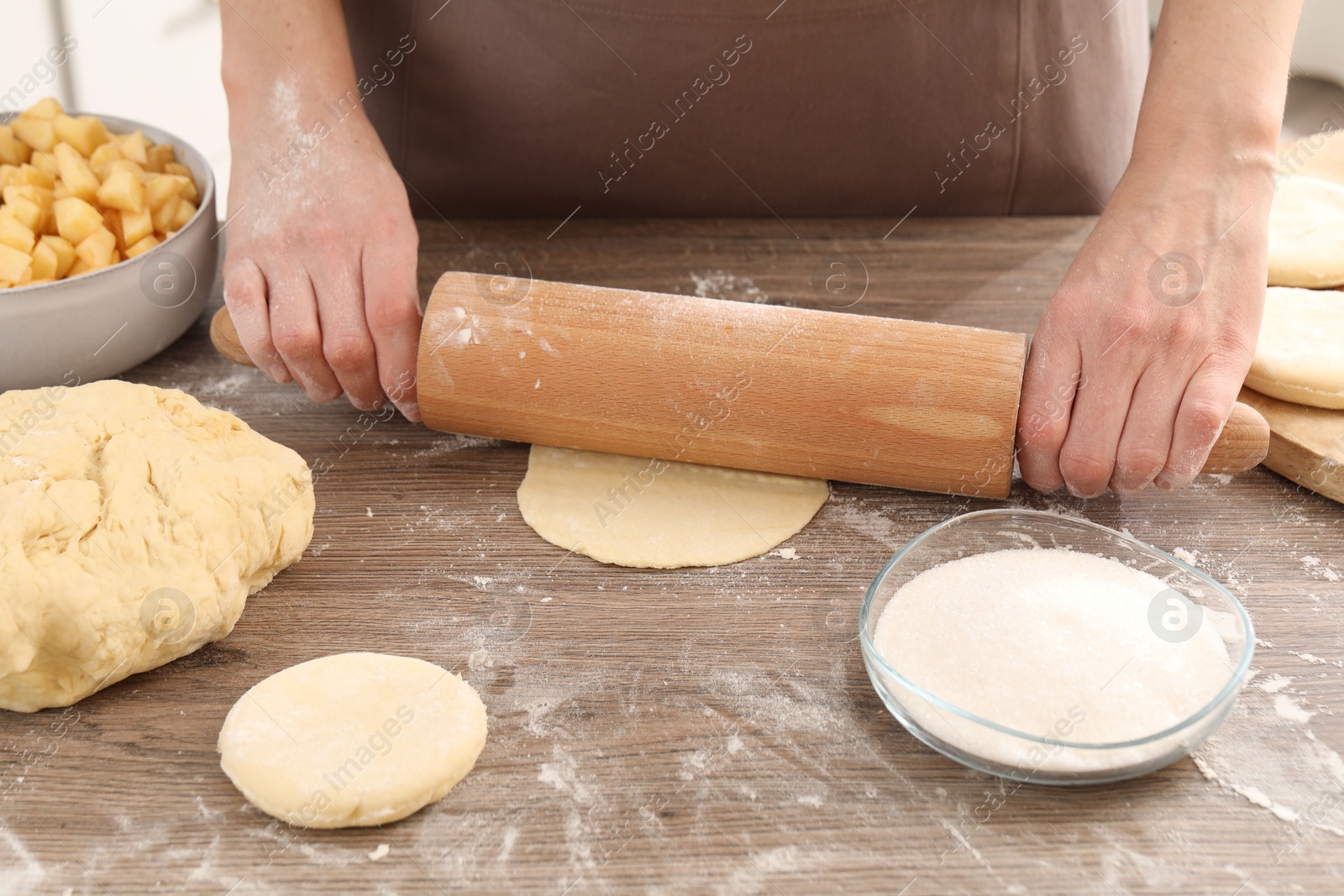 Photo of Making pirozhki (stuffed pastry pies). Woman shaping dough with rolling pin at wooden table, closeup