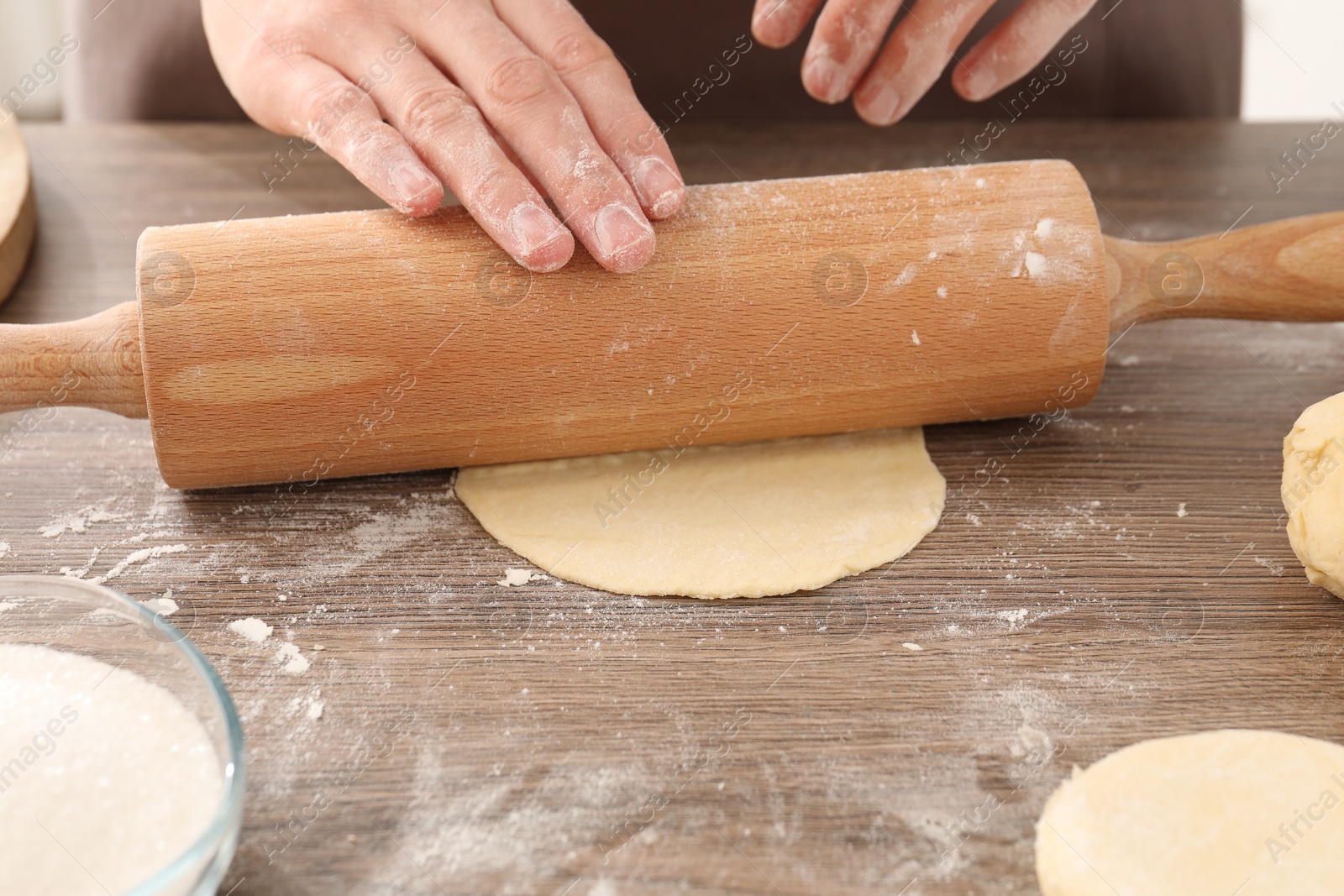 Photo of Making pirozhki (stuffed pastry pies). Woman shaping dough with rolling pin at wooden table, closeup