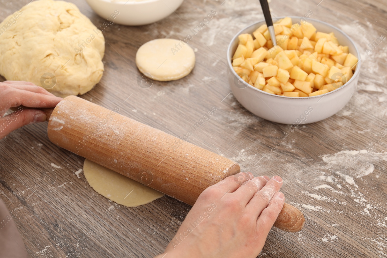 Photo of Making pirozhki (stuffed pastry pies). Woman shaping dough with rolling pin at wooden table, closeup