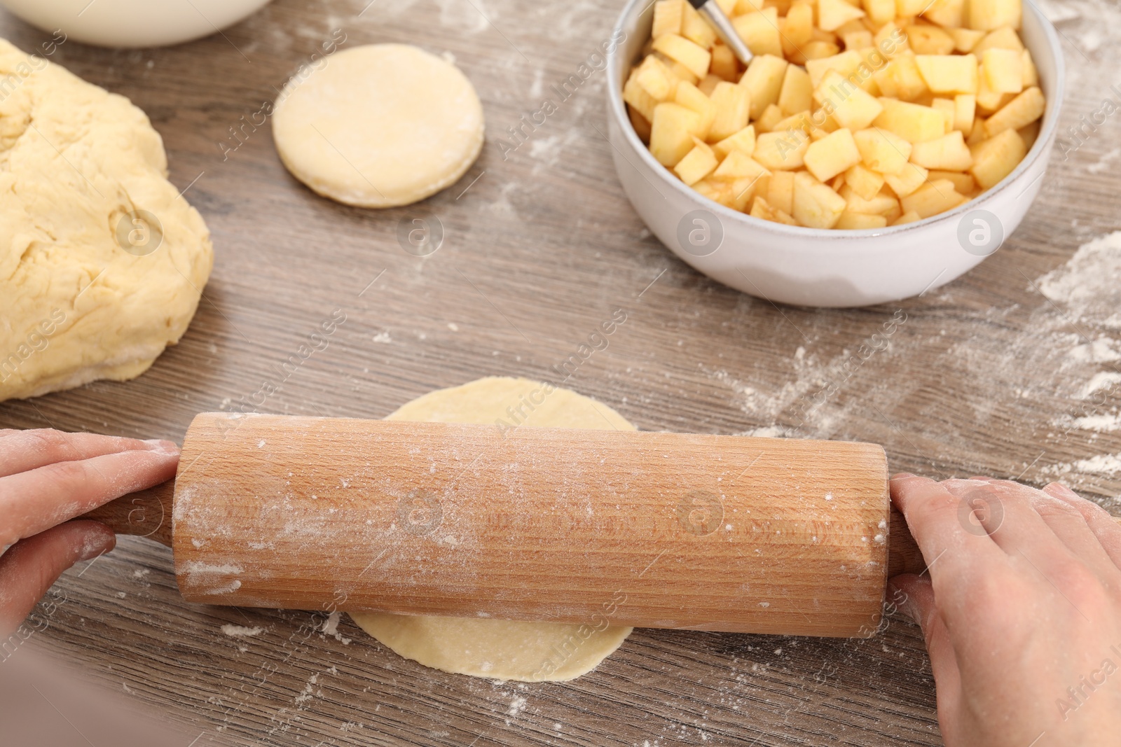 Photo of Making pirozhki (stuffed pastry pies). Woman shaping dough with rolling pin at wooden table, closeup