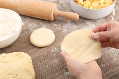 Photo of Making pirozhki (stuffed pastry pies). Woman with dough at wooden table, closeup