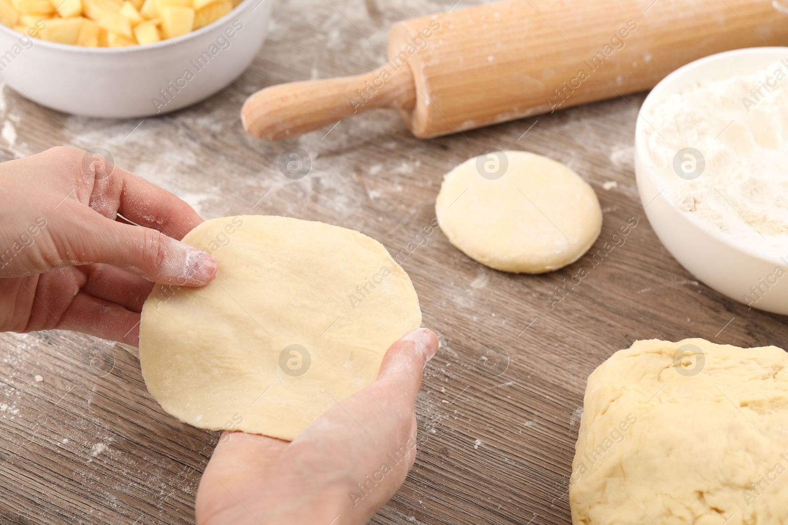 Photo of Making pirozhki (stuffed pastry pies). Woman with dough at wooden table, closeup